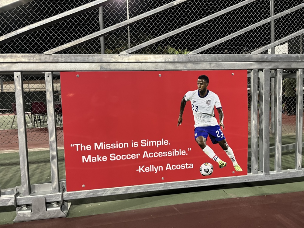 A sign with a photo of Kellyn that reads, "The mission is simple. Make soccer accessible." - Kellyn Acosta